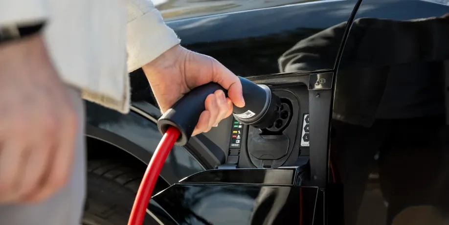 Hand einer Person trennt den Ladestecker mit rotem Kabel von der Ladeklappe eines schwarzen Elektroautos, Schritt 3 der Ladeanleitung für AC-Laden.