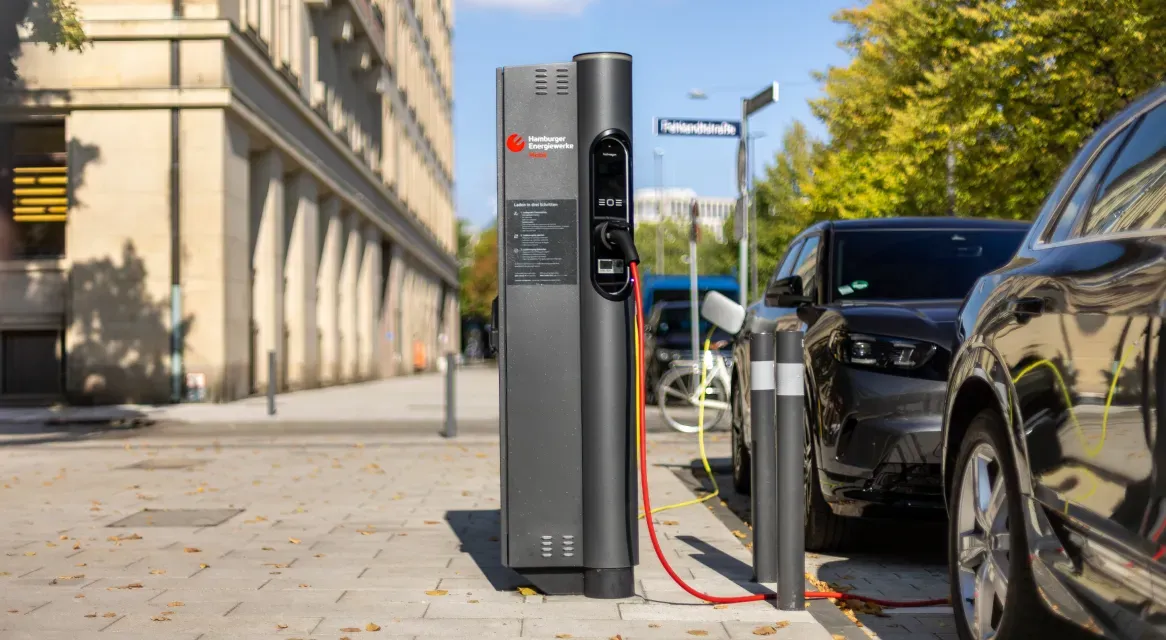 Elektroauto lädt an einer öffentlichen Ladesäule am Straßenrand in Hamburg, weitere parkende Fahrzeuge und Häuserfassaden im Hintergrund.