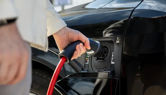Hand einer Person trennt den Ladestecker mit rotem Kabel von der Ladeklappe eines schwarzen Elektroautos, Schritt 3 der Ladeanleitung für AC-Laden.