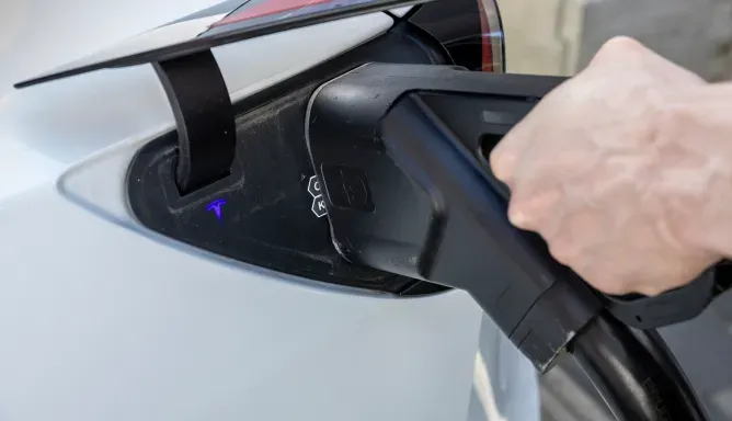 Hand einer Person steckt einen großen DC-Schnellladestecker in den Ladeanschluss eines Elektroautos, Schritt 2 der Ladeanleitung für DC-Laden.