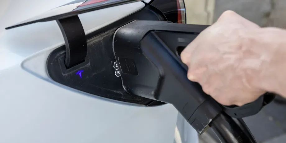 Hand einer Person steckt einen großen DC-Schnellladestecker in den Ladeanschluss eines Elektroautos, Schritt 2 der Ladeanleitung für DC-Laden.