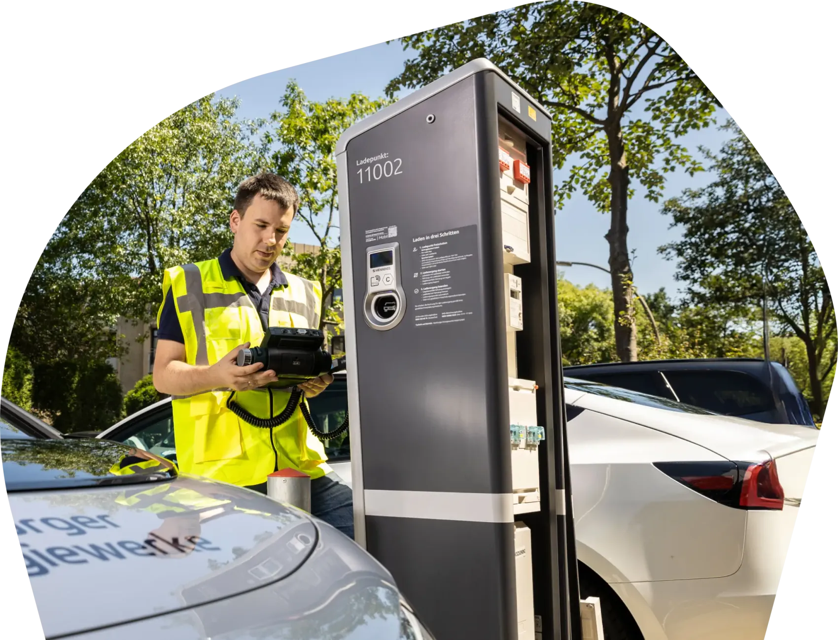 Mitarbeitende Person in gelber Warnweste steht mit einem Prüfgerät an einer öffentlichen Ladesäule, im Vordergrund ist ein Dienstfahrzeug zu sehen; daneben der Text „Arbeiten bei HEnW Mobil – Lust auf eine nachhaltige Karriere? Dann gestalte mit uns einen wesentlichen Teil der Hamburger Mobilitäts- und Energiewende!“.