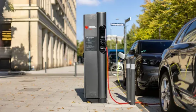 Elektroauto lädt an einer öffentlichen Ladesäule am Straßenrand in Hamburg, weitere parkende Fahrzeuge und Häuserfassaden im Hintergrund.