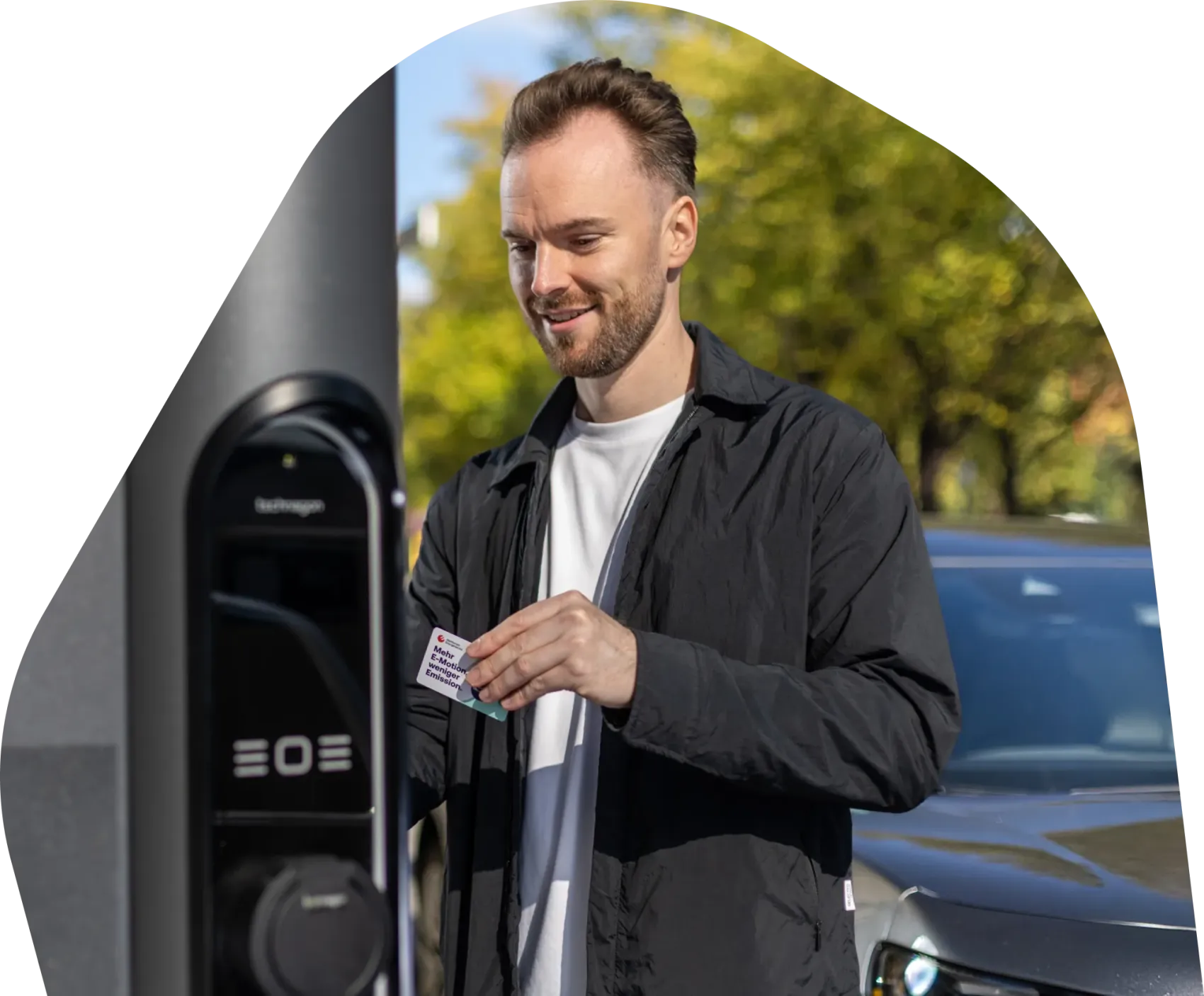 Person steht an einer öffentlichen Ladesäule und hält eine Ladekarte in der Hand, daneben der Text „Wir elektrisieren Hamburg. Wir machen Elektromobilität möglich für alle, die in unserer schönen Stadt leben oder sie besuchen.“