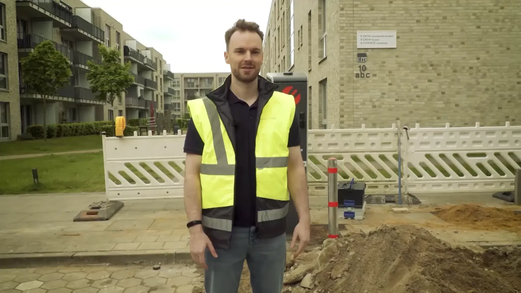Mitarbeiter in Warnweste steht auf einer Baustelle mit aufgerissenem Gehweg und Absperrungen vor Wohngebäuden, darüber der Text „Gemeinsam die Zukunft der Mobilität gestalten“ und ein Button „Video starten“.