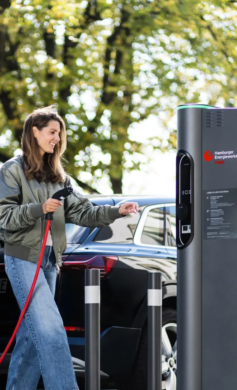 Person lädt ein Elektroauto an einer öffentlichen Ladesäule von Hamburg Energie, im Hintergrund stehen weitere Fahrzeuge. Text im Bild: „Elektromobilität für Hamburg“ und ein Button „Mehr erfahren zur Mission“.